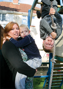 Steph, holding one of her sons, another son is upside down on a climbing frame beside them